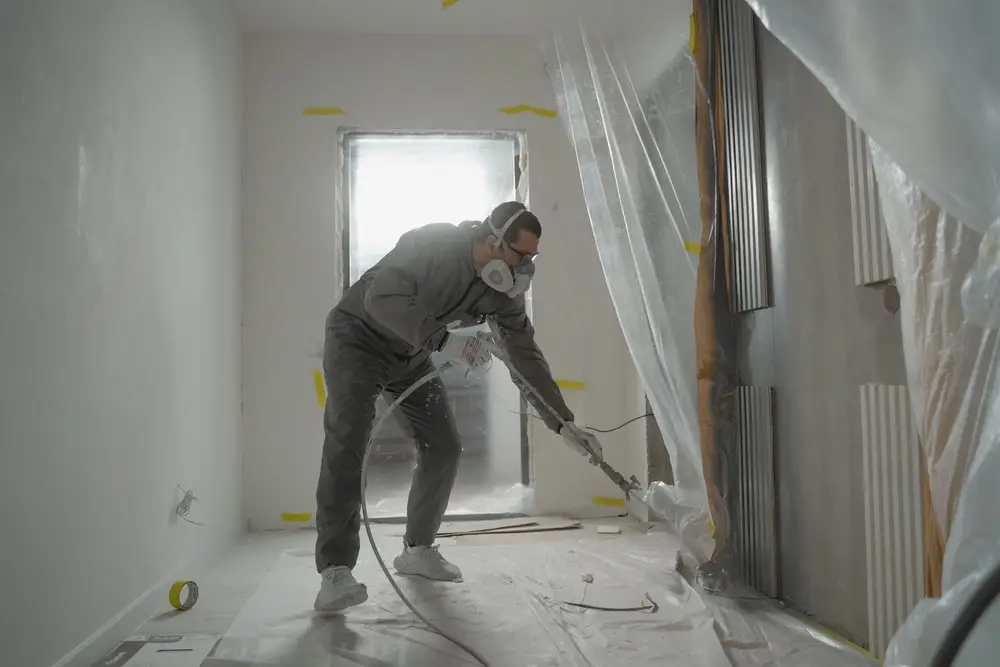 Painter spraying walls in a room covered with plastic sheeting