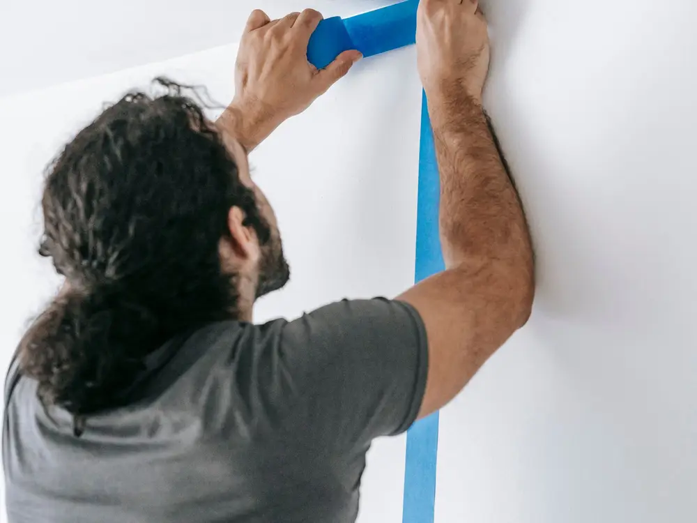 Painter pressing tape along a wall before painting