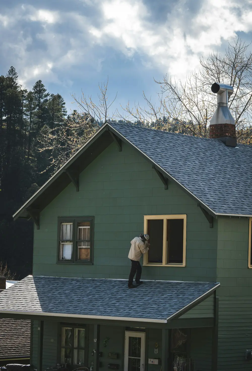 Painter working on the roof trim of a green house